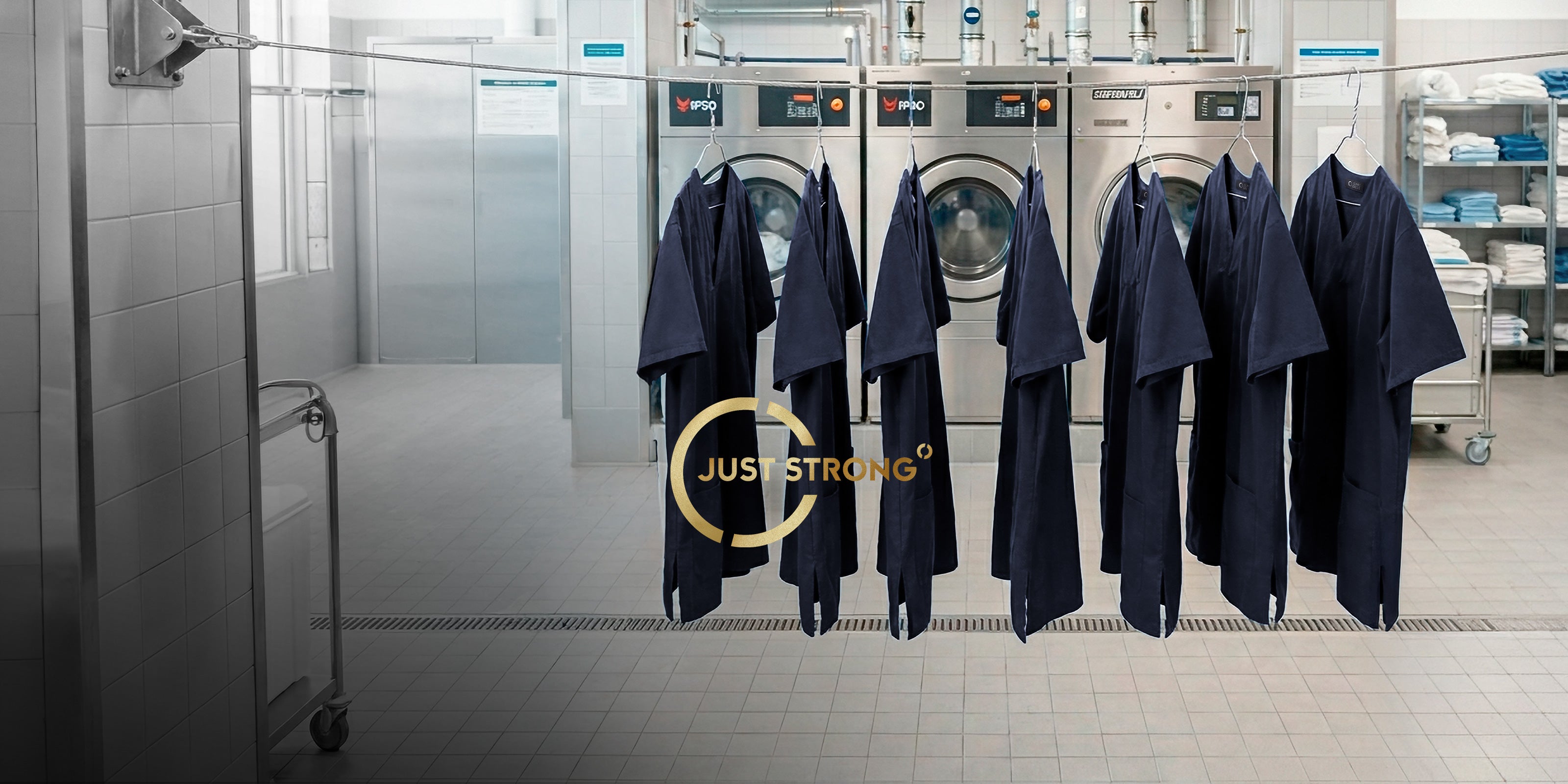 Donkerblauwe JUST STRONG werkjassen op kledinghangers voor industriële wasmachines in een wasserij.